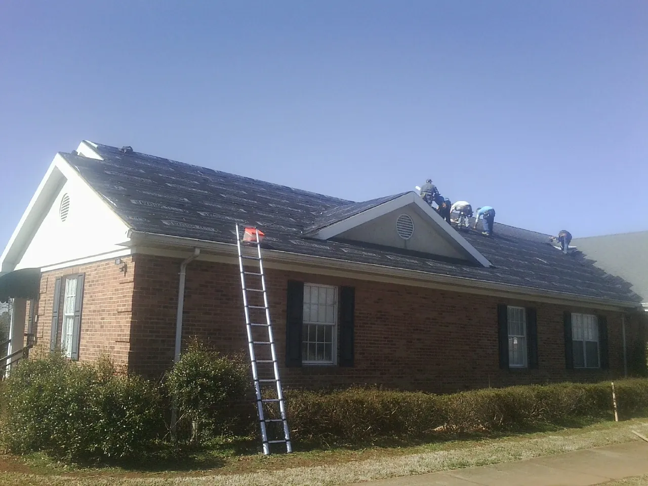 Crew tearing shingles off a brick ranch roof with a ladder set — Emergency Roof Repair work by our crew in Saugatuck