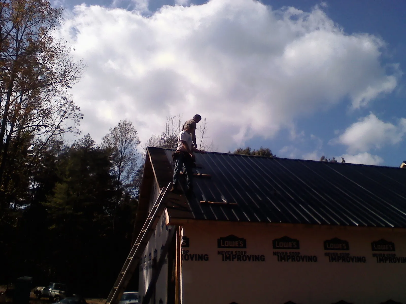 Roofer fastening dark metal panels high against a cloudy sky, from a Roof Inspection job in Saugatuck