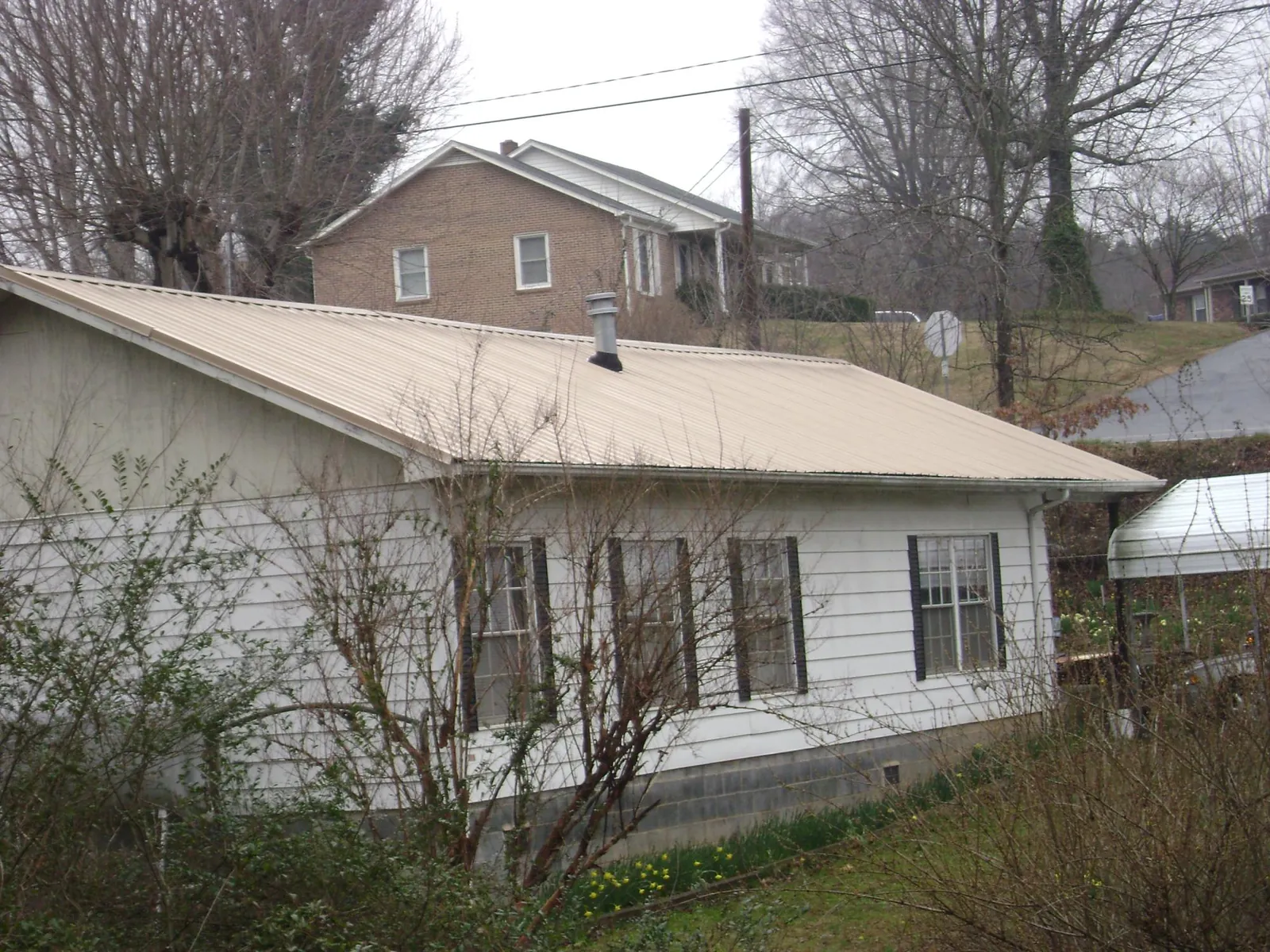 Tan metal roof on a white sided house set into a hillside — Commercial Roofing by Roofing Brothers in Saugatuck