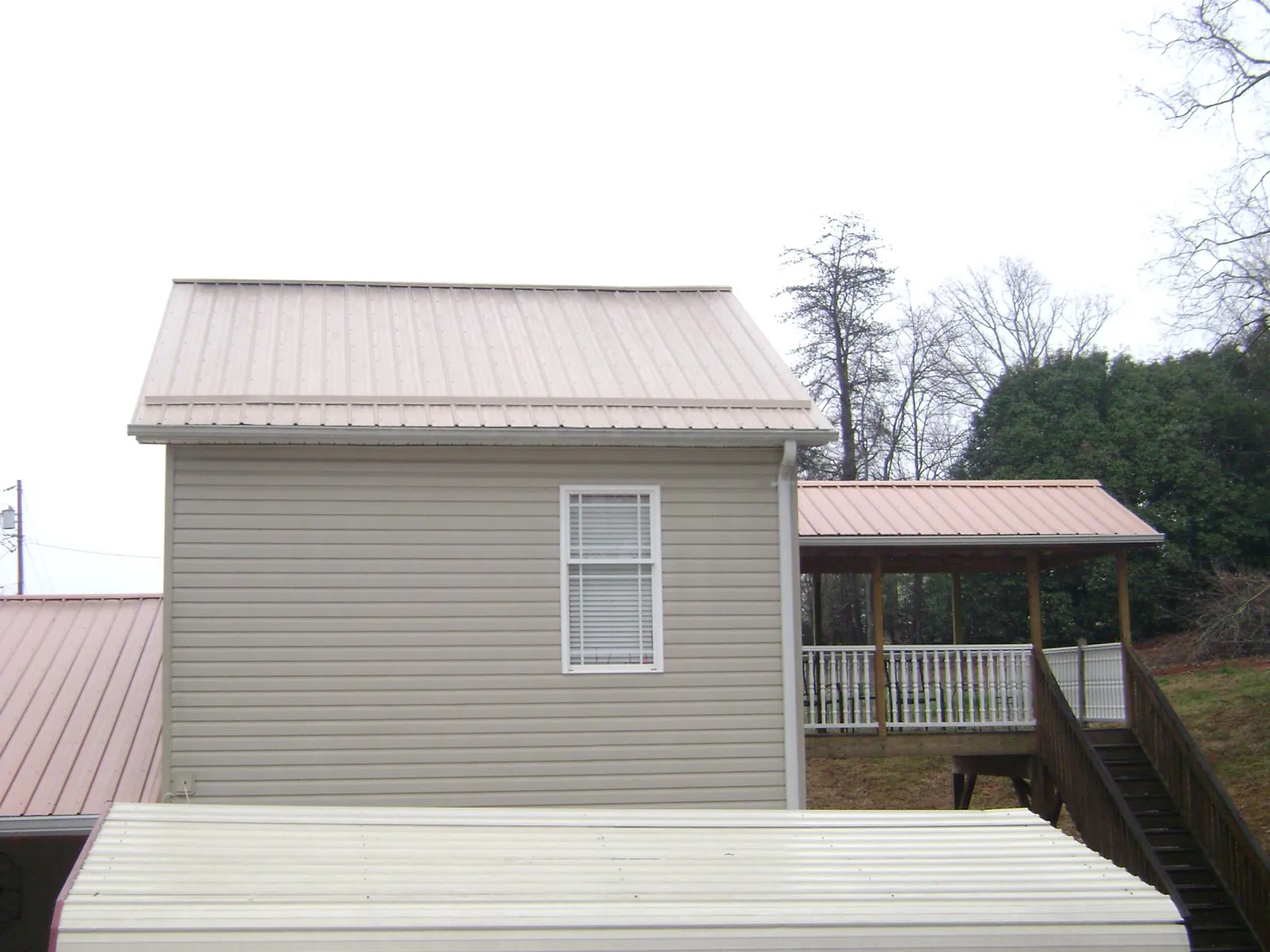 Tan metal roofs on a two story addition and attached porch, from a Roof Replacement job in Saugatuck